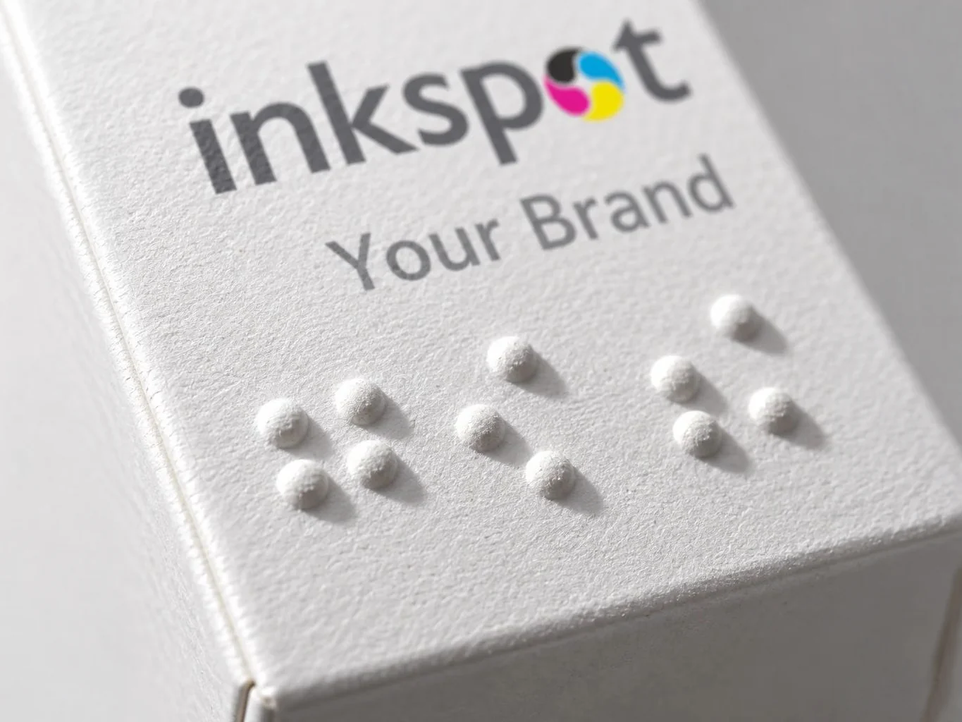 Close up of raised braille dots embossed on a white carton below the printed brand name.